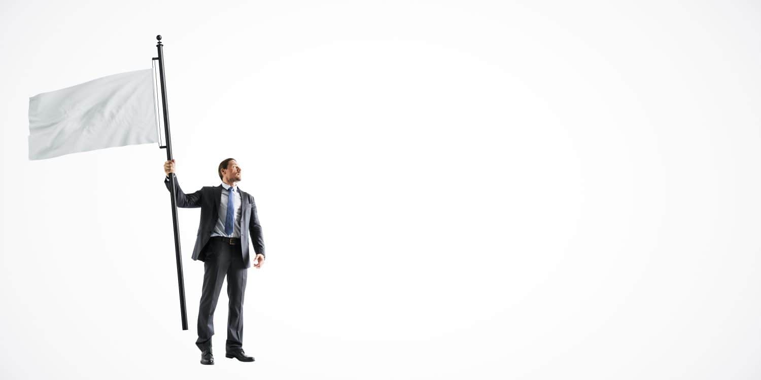 Businessman in a suit holding a large white flagpole, standing on a light white background. Concept of surrender, peace, or marketing