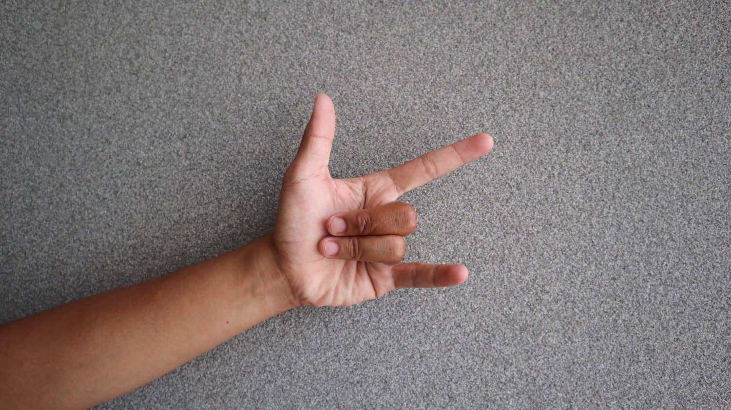 Rocker hand showing horns or rock gesture. Man&#039;s hand gesturing rock and roll, heavy metal, devil horns gesture or I love you on grery background