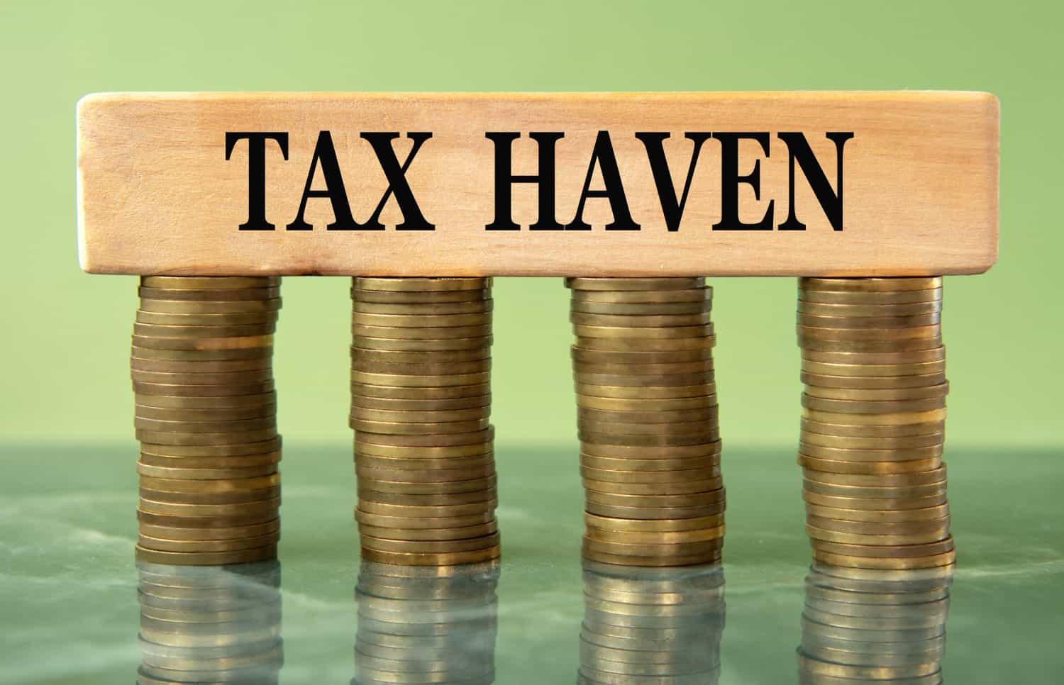 TAX HAVEN - words on a wooden block on a background of stacks of coins