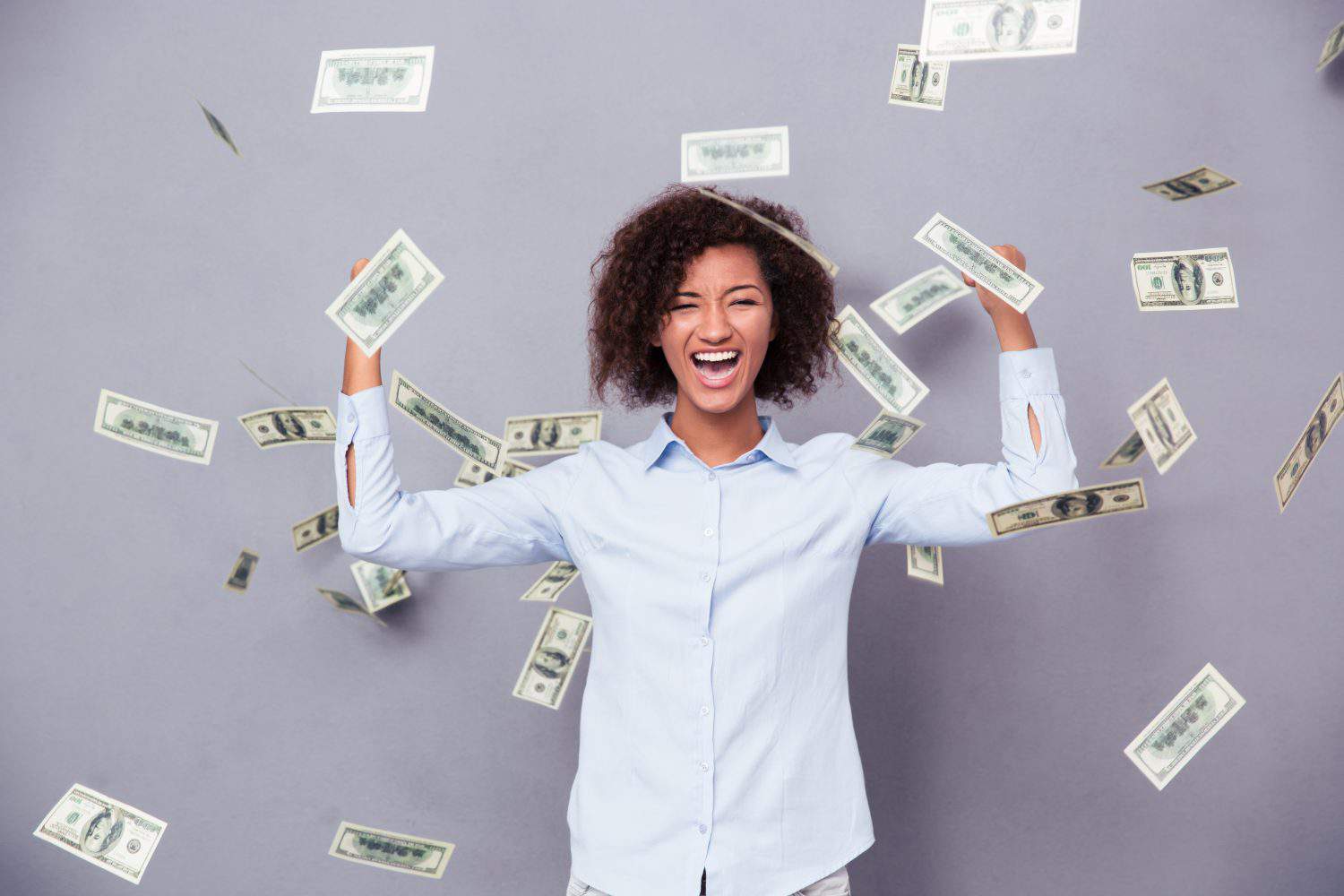 Concept photo of a cheerful afro american woman standing under rain with money on gray background