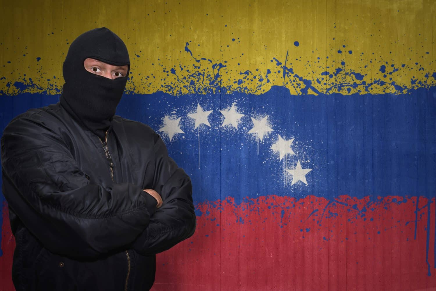 dangerous man in a mask standing near a wall with painted national flag of venezuela