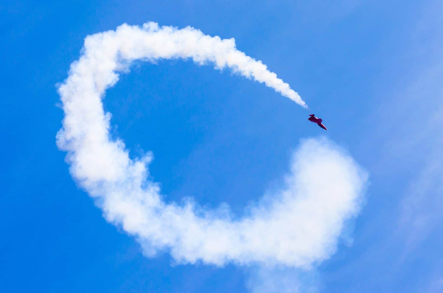 Red combat fighter with white circle smoke behind in the blue sky.