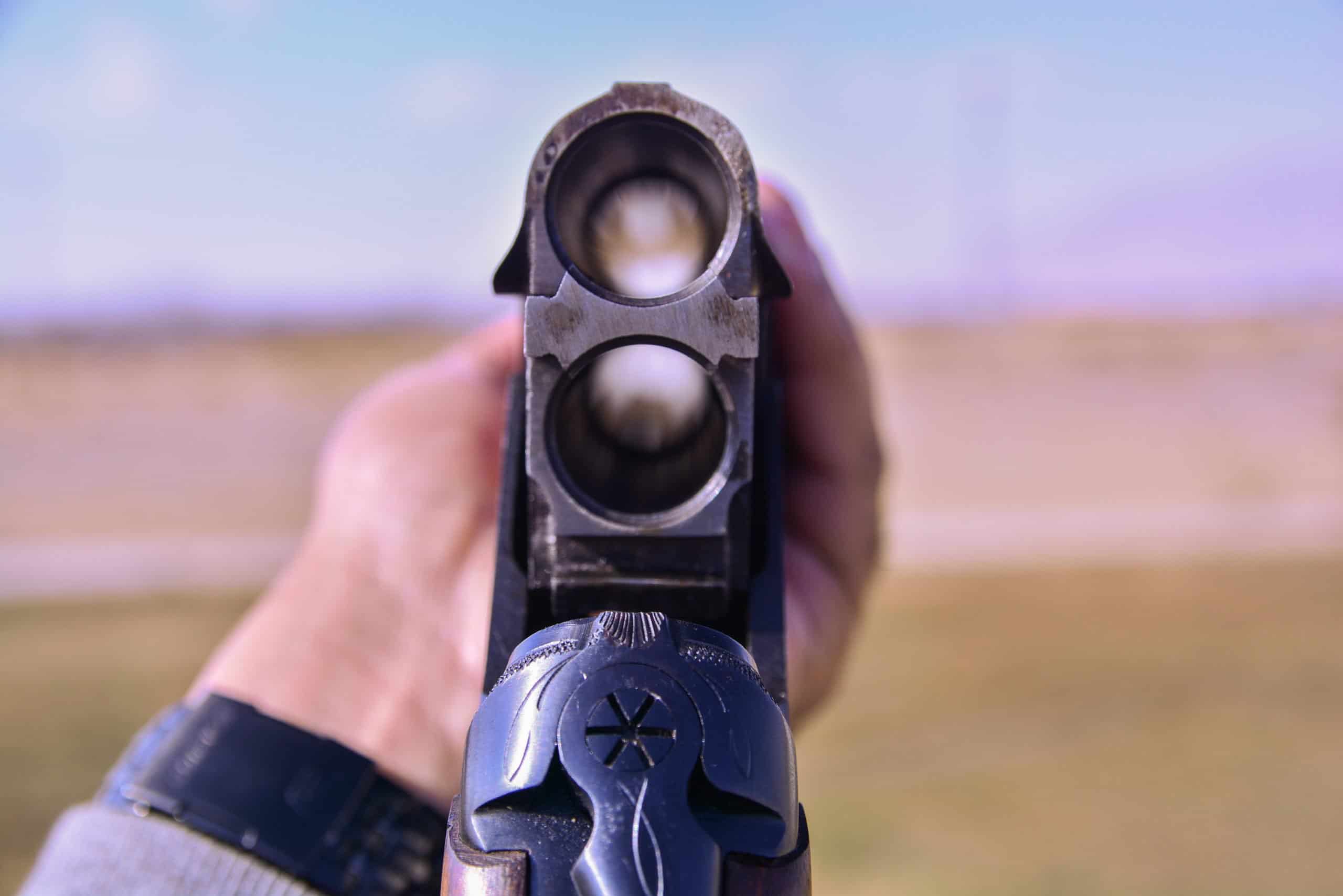 A man holding a shot gun gun empty gun with two barrels with cartridges and aiming towards target at the skeet shooting range.