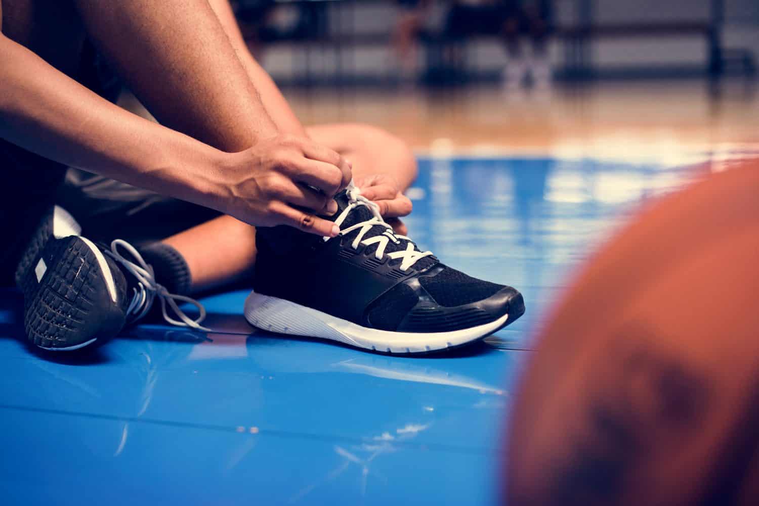 African American teenage boy tying his shoe laces on a basketball court