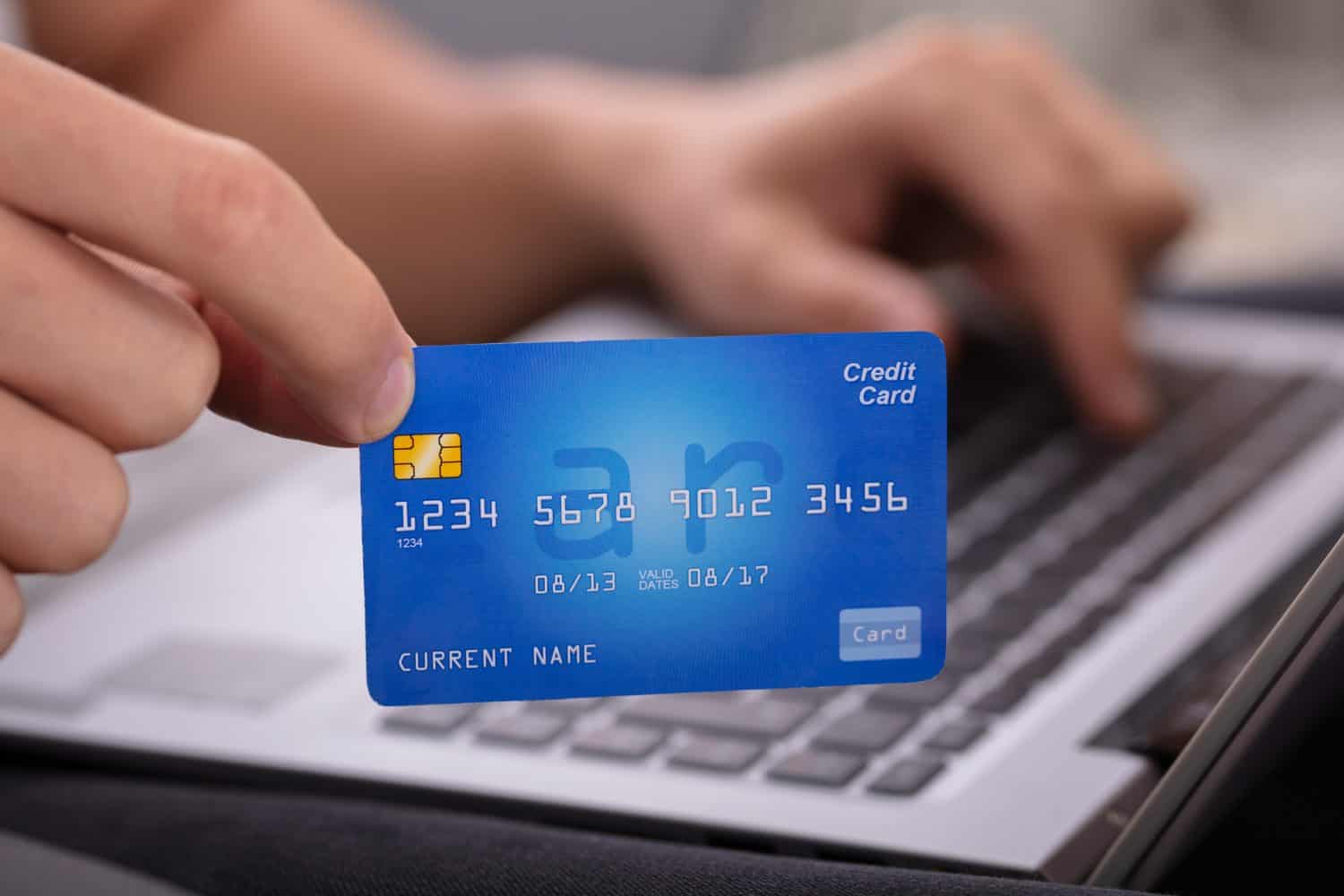 Close-up Of A Man&#039;s Hand Holding Credit Card While Shopping Online On Laptop