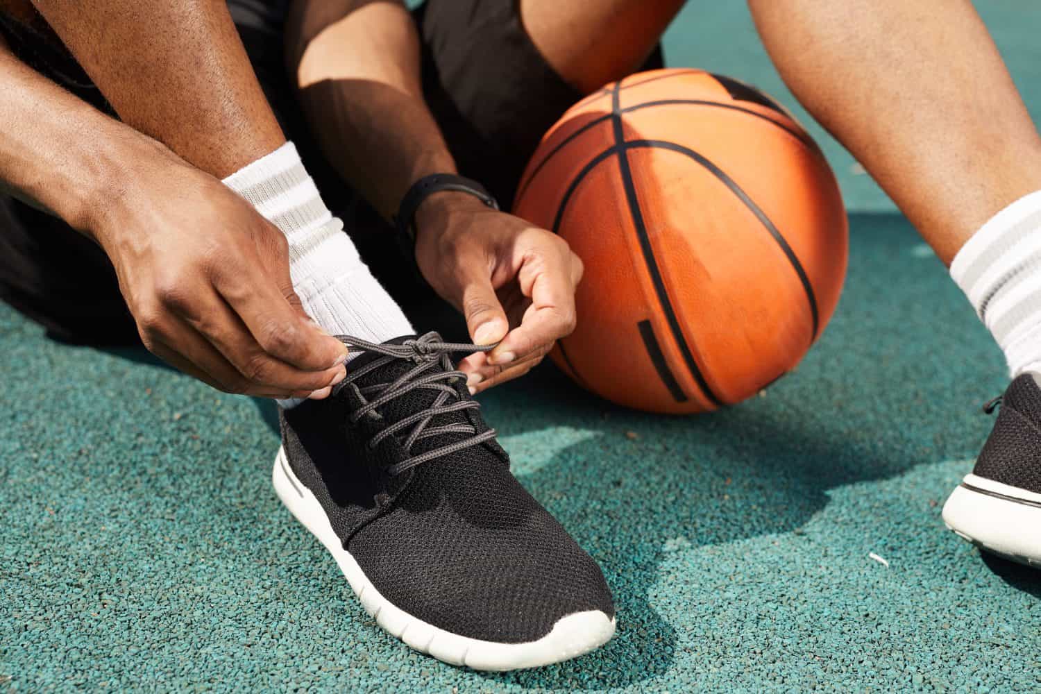 Closeup of African-American man tying sports shoes in basketball court outdoors, copy space background