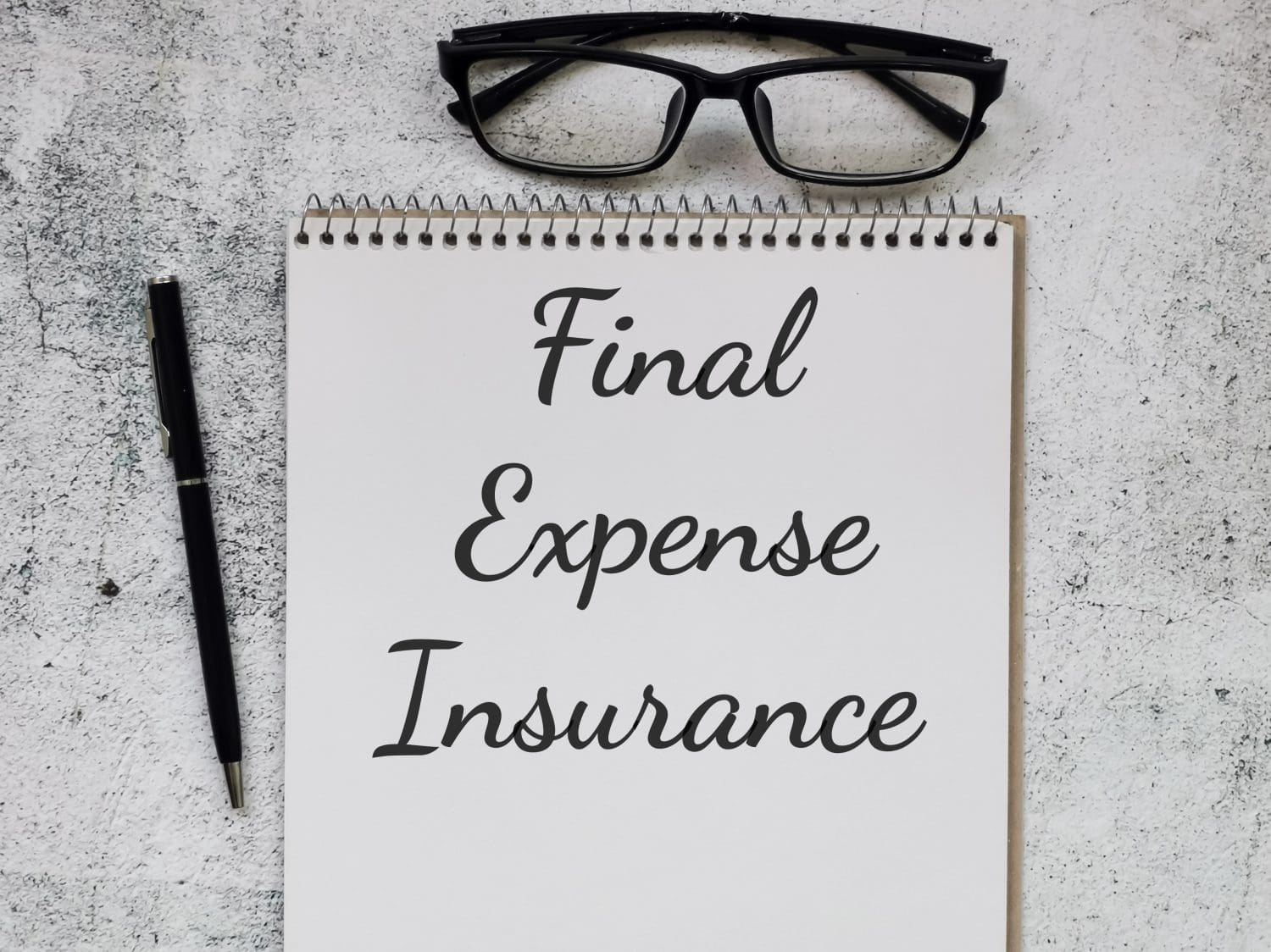 Phrase Final Expense Insurance written on note book with pen and eye glasses. Business concept.