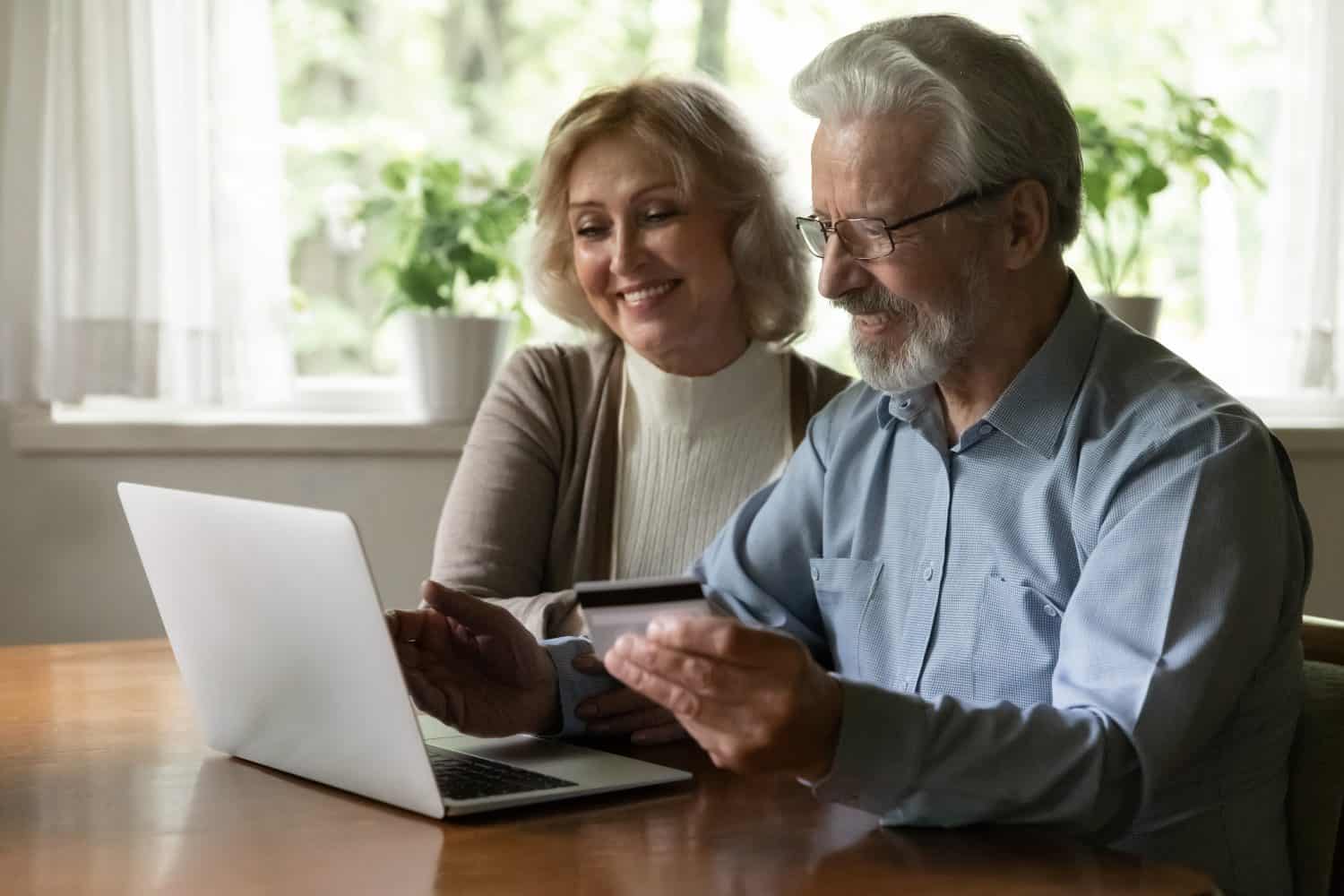 Close up smiling mature man and woman paying online by plastic credit card together, using laptop, shopping at home, satisfied elderly customers making secure internet payment, checking balance