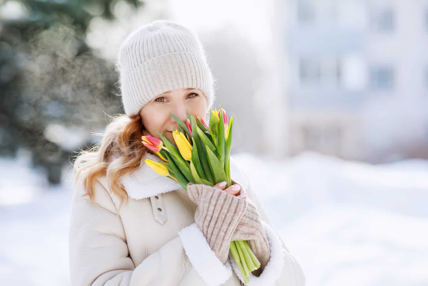 A girl with a bouquet of yellow and pink tulips on a walk on a sunny winter day. Flowers for International Women&#039;s Day. The nature of Siberia in Russia.