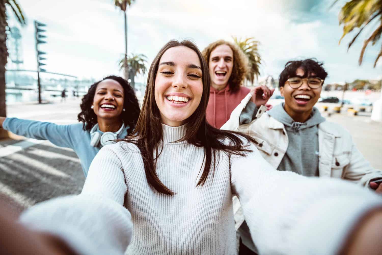 Young people taking selfie photo with smart mobile phone outside - Multicultural friends running on city street enjoying freedom - Happy students celebrating summer holidays