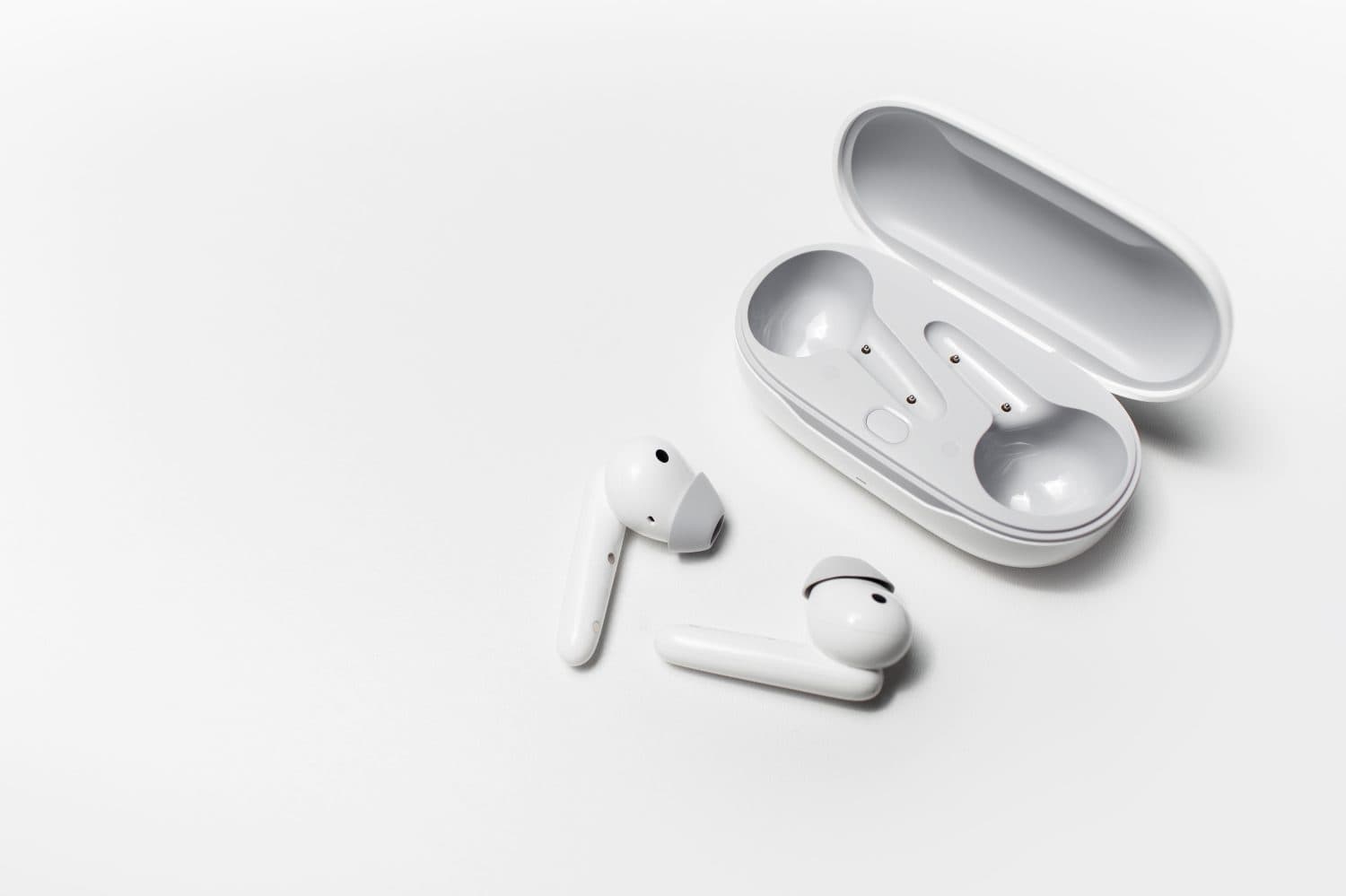 Close-up of modern wireless earphones lying near opened charging case on white background with copy space.