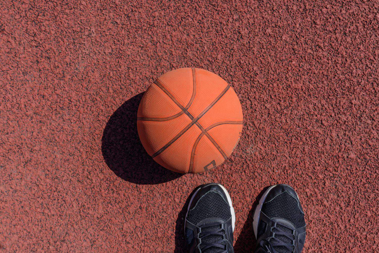 Basketball ball,sneakers lying on the rubber sport court.Sport red ground outdoor.Top view,Copy space.