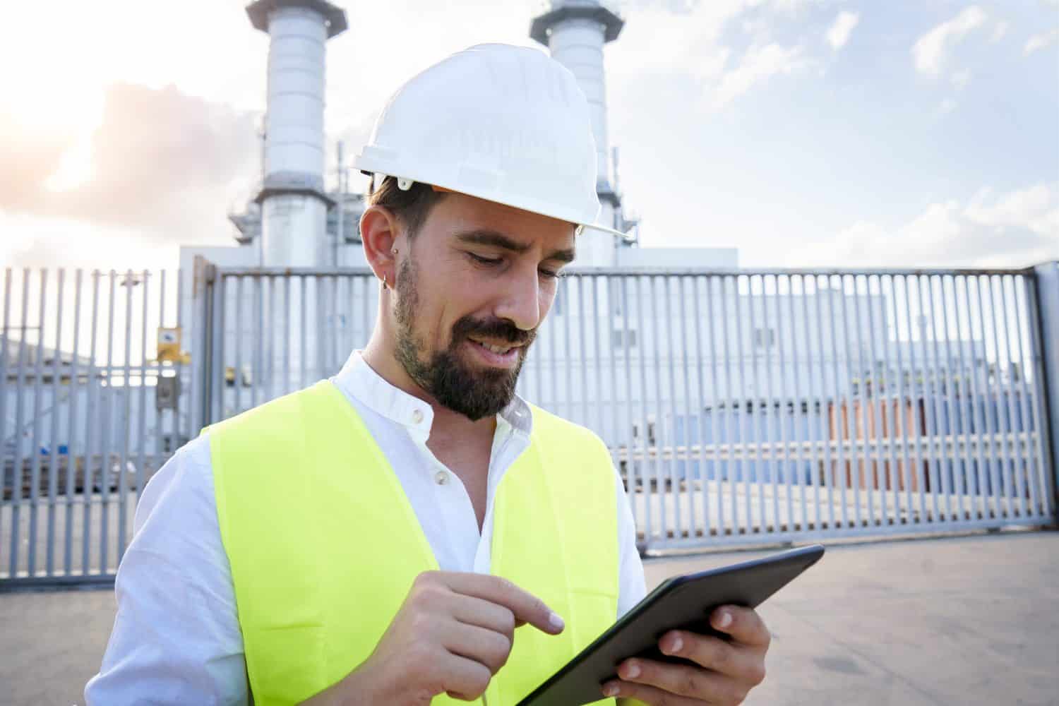 Close up portrait of a caucasian engineer using digital tablet to do an inspection at thermoelectric plant. Worker outside power station introducing data to an electronic device. High quality photo