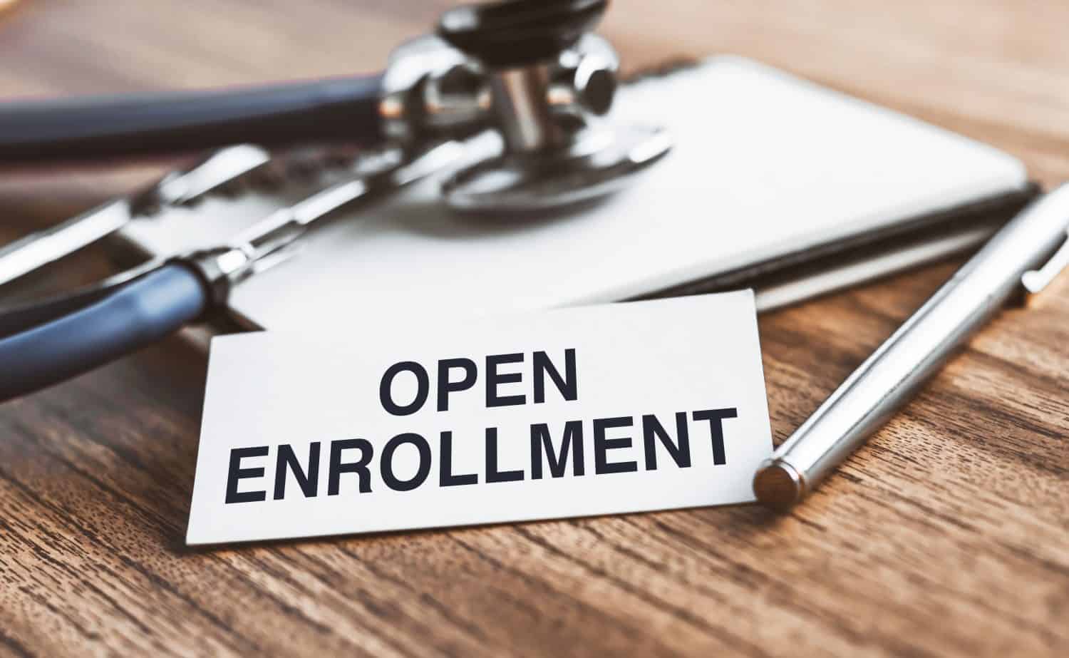 The text open enrollment is written on notepad near a stethoscope on a wooden background. Medical concept