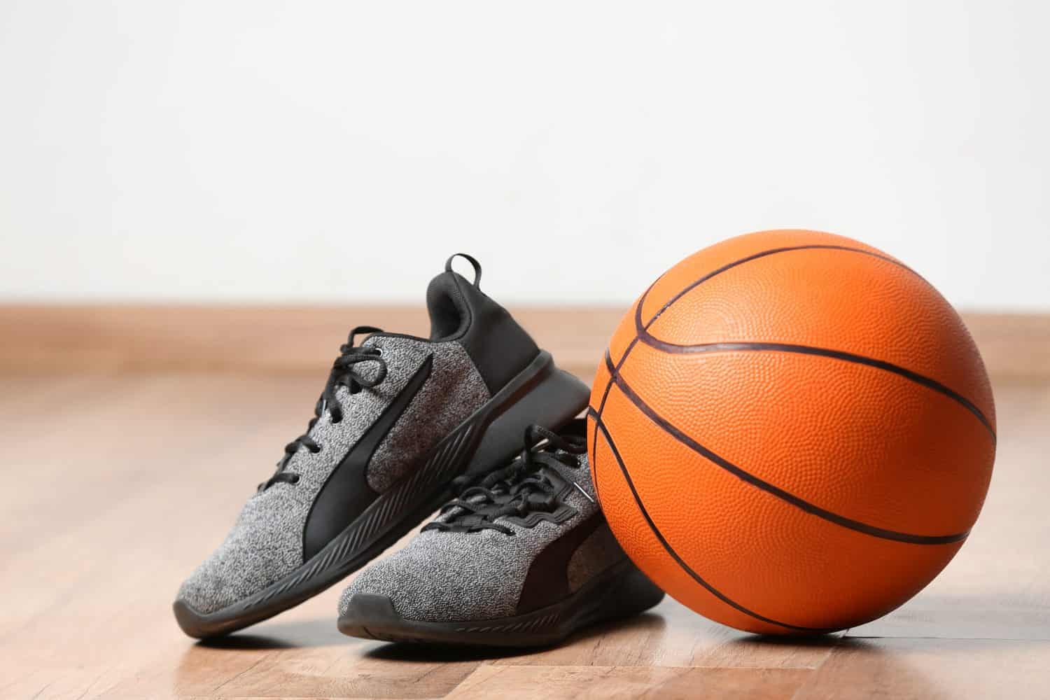 Trainers and ball for playing basketball on floor near white wall