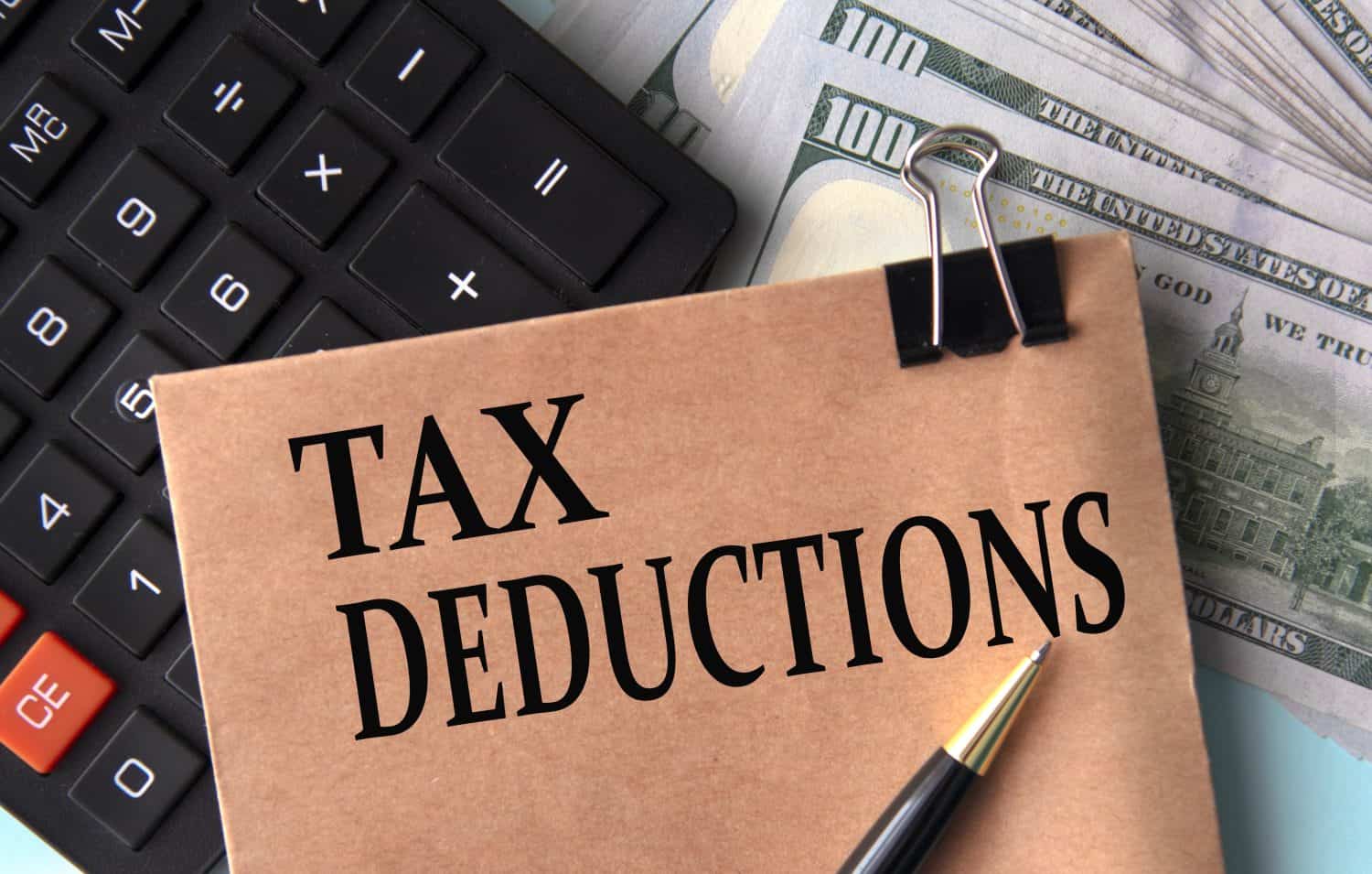 TAX DEDUCTIONS - words on brown paper on the background of calculator and banknotes. Business concept