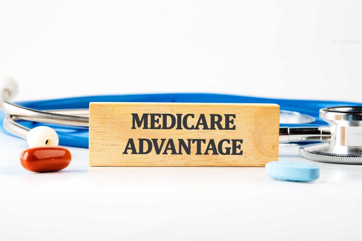 Medicare Advantage text on a wooden block with a stethoscope lying next to it, pills, vitamins on a white background