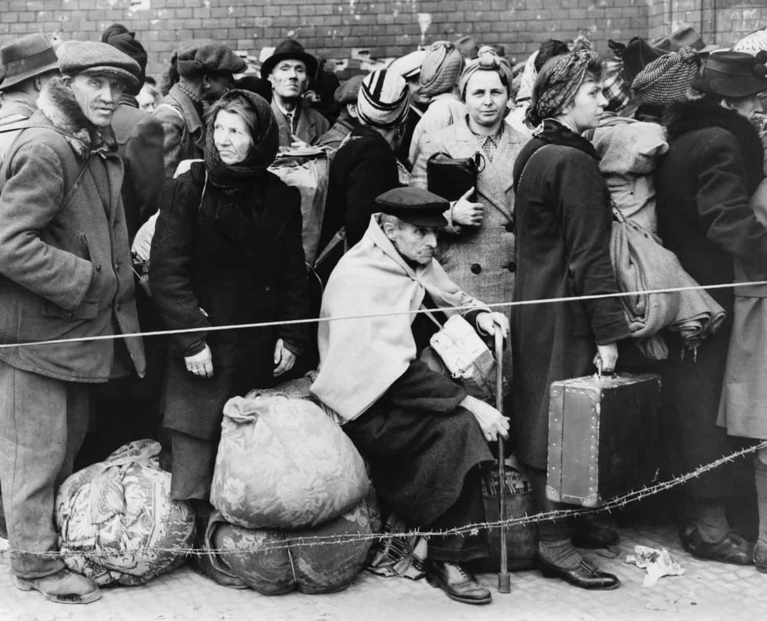 German displaced persons wait in Berlin&#039;s Anhalter Station in 1945. Refugees are carrying their few belongings, as the stand behind a rope and double strand of barbed wire.