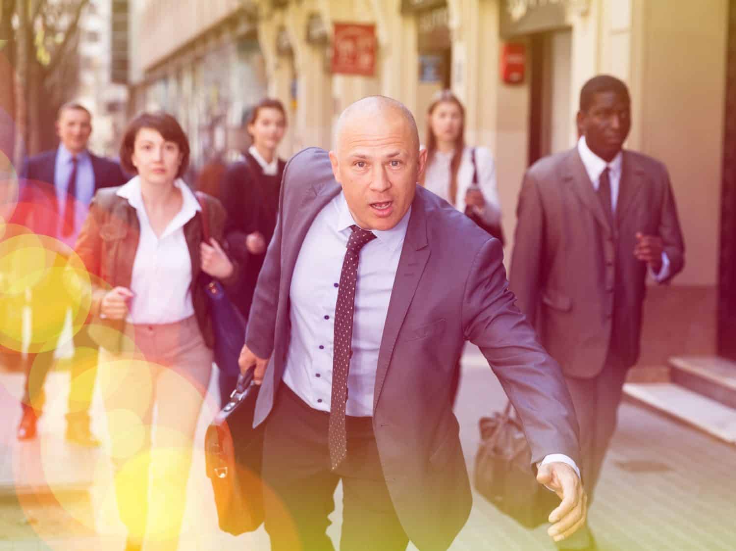 Hurrying businessman in formal suit with briefcase in hand running on city street in crowd of people.