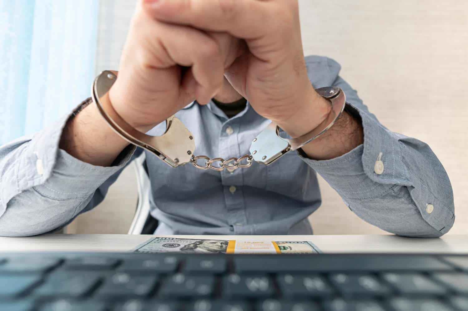 a man in handcuffs is sitting at his workplace with a computer and money in dollars.. The concept of bribery and criminal crimes in the cyber sphere. internet censorship