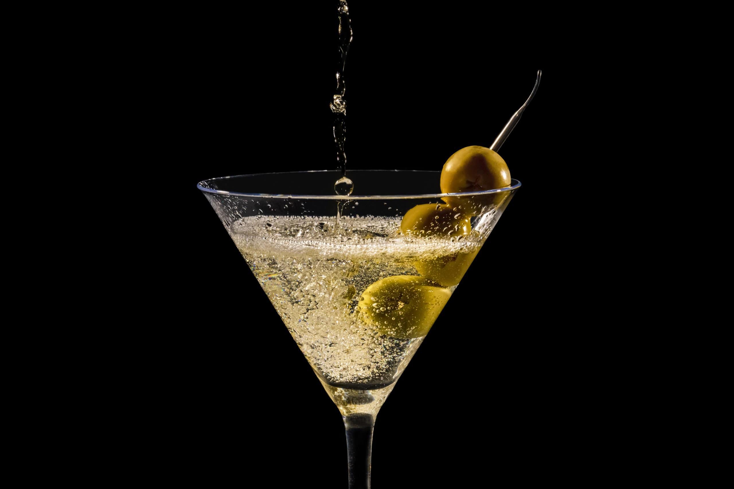 Close up of pouring and splashing  martini glass with olives