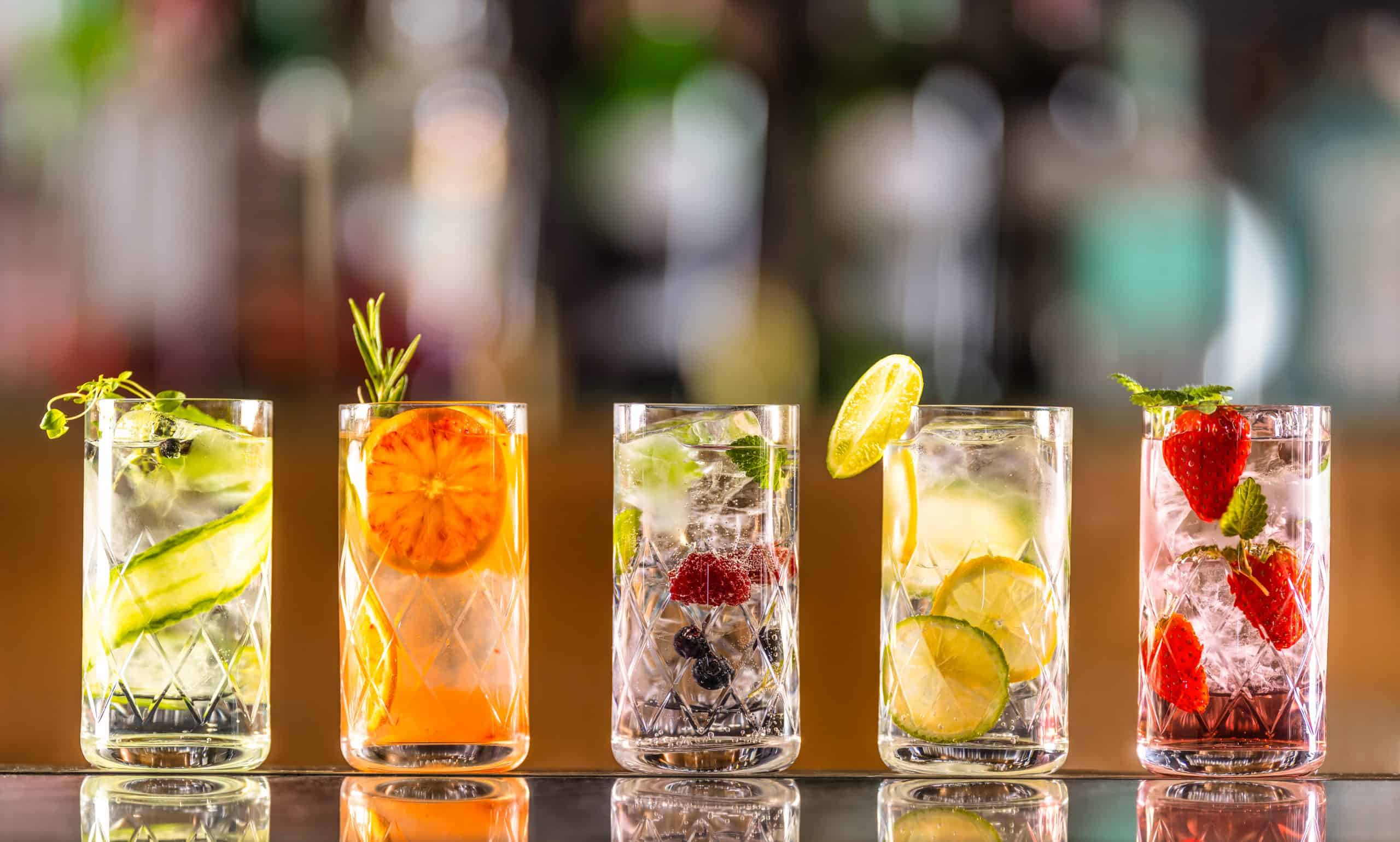 Five gin tonic cocktails in wine glasses on bar counter in pup or restaurant.