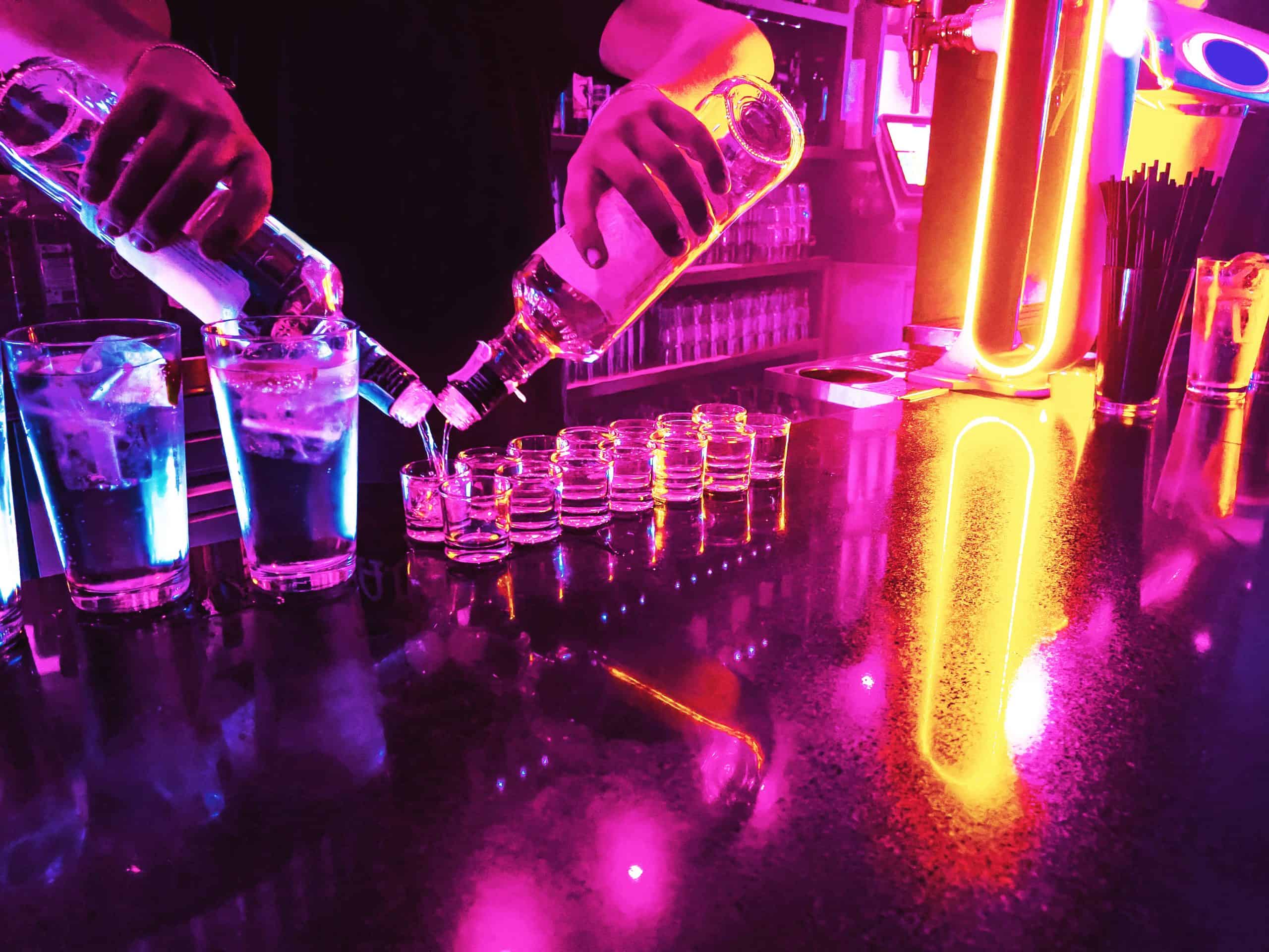 Bartender serving alcohol shots in neon illuminated bar.