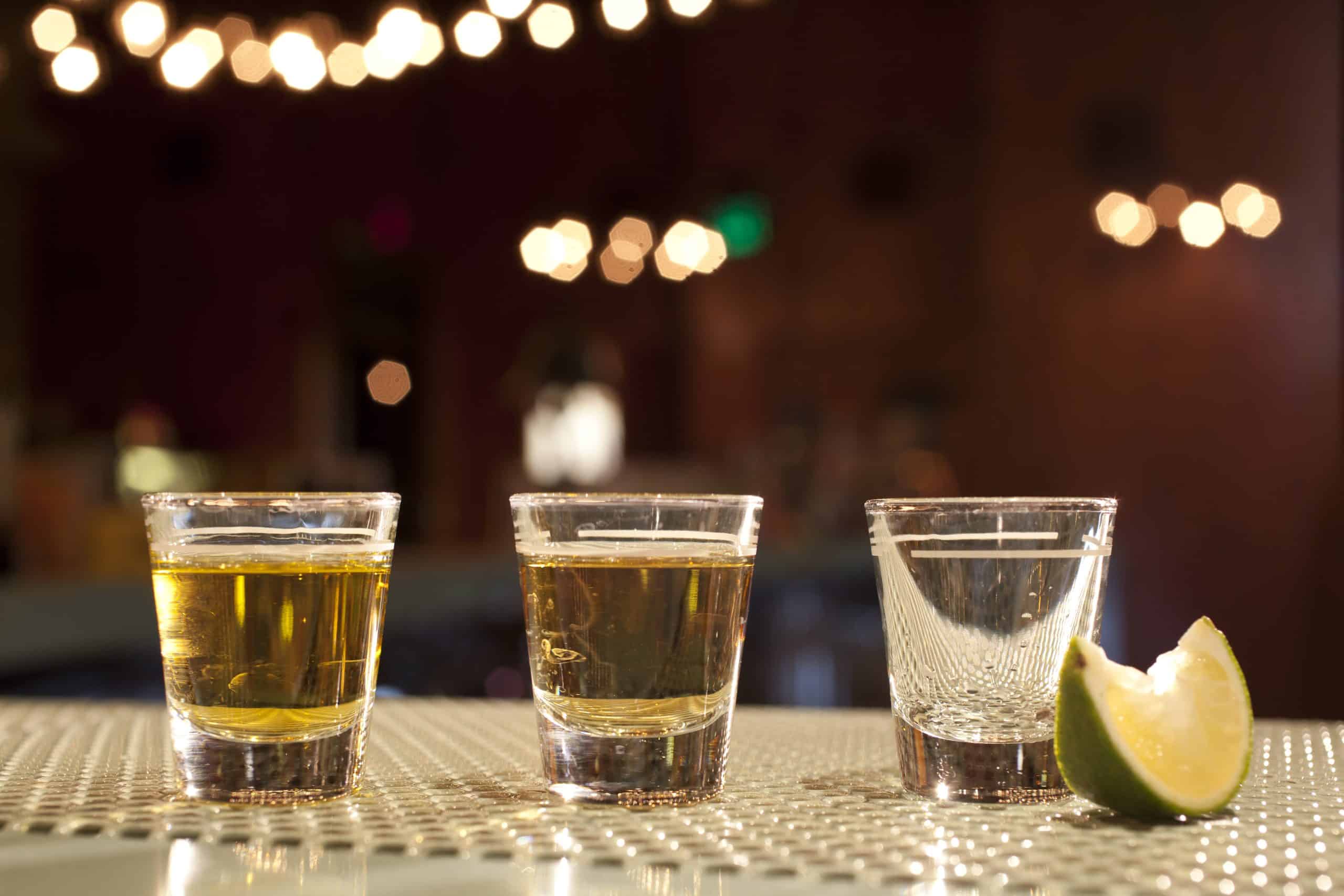 Shots of various types of tequila on bar with lime wedge