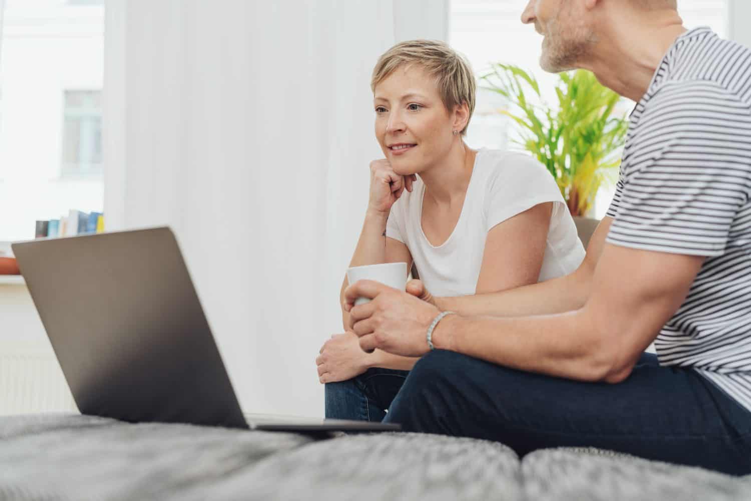 Middle-aged couple relaxing on a sofa with coffee and an open laptop with focus to the thoughtful woman staring at the screen