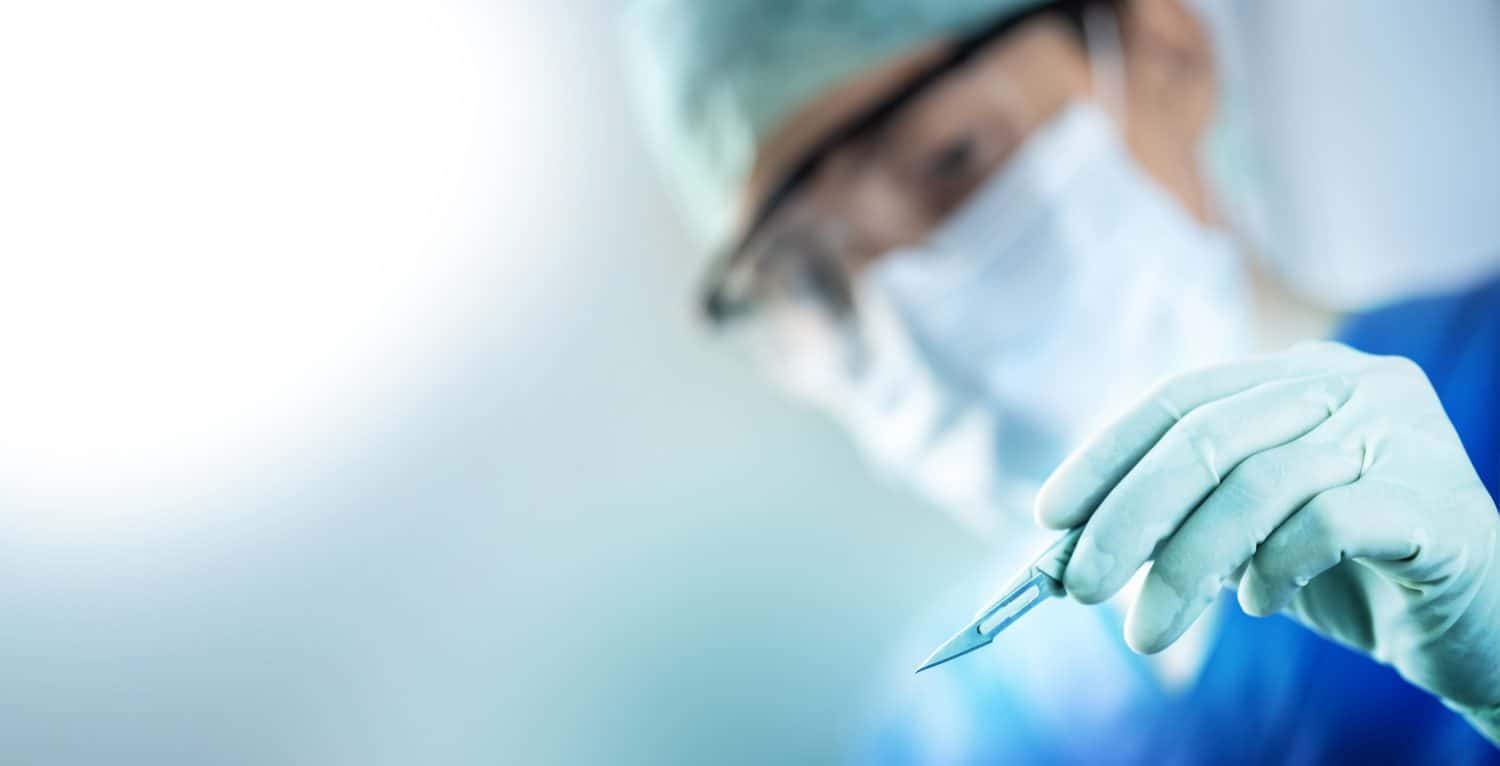 close up of the surgeon&#039;s hand holding a scalpel and blurred female doctor&#039;s face in the background with copy space, concept of surgical operations, hospitals and clinic staff