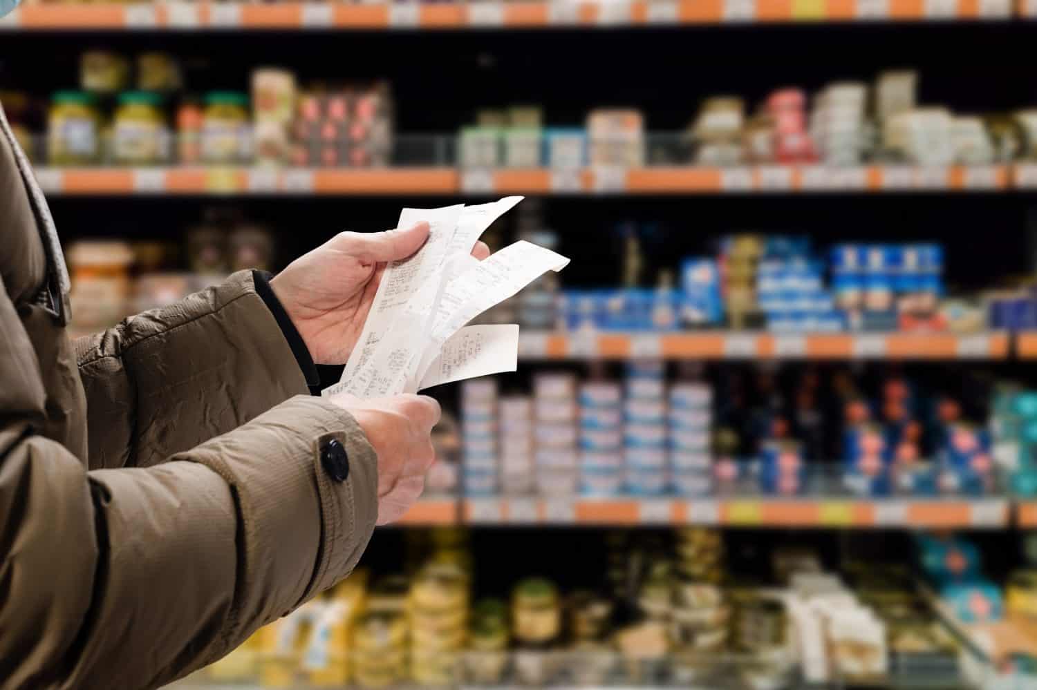 Minded man viewing receipts in supermarket and tracking prices