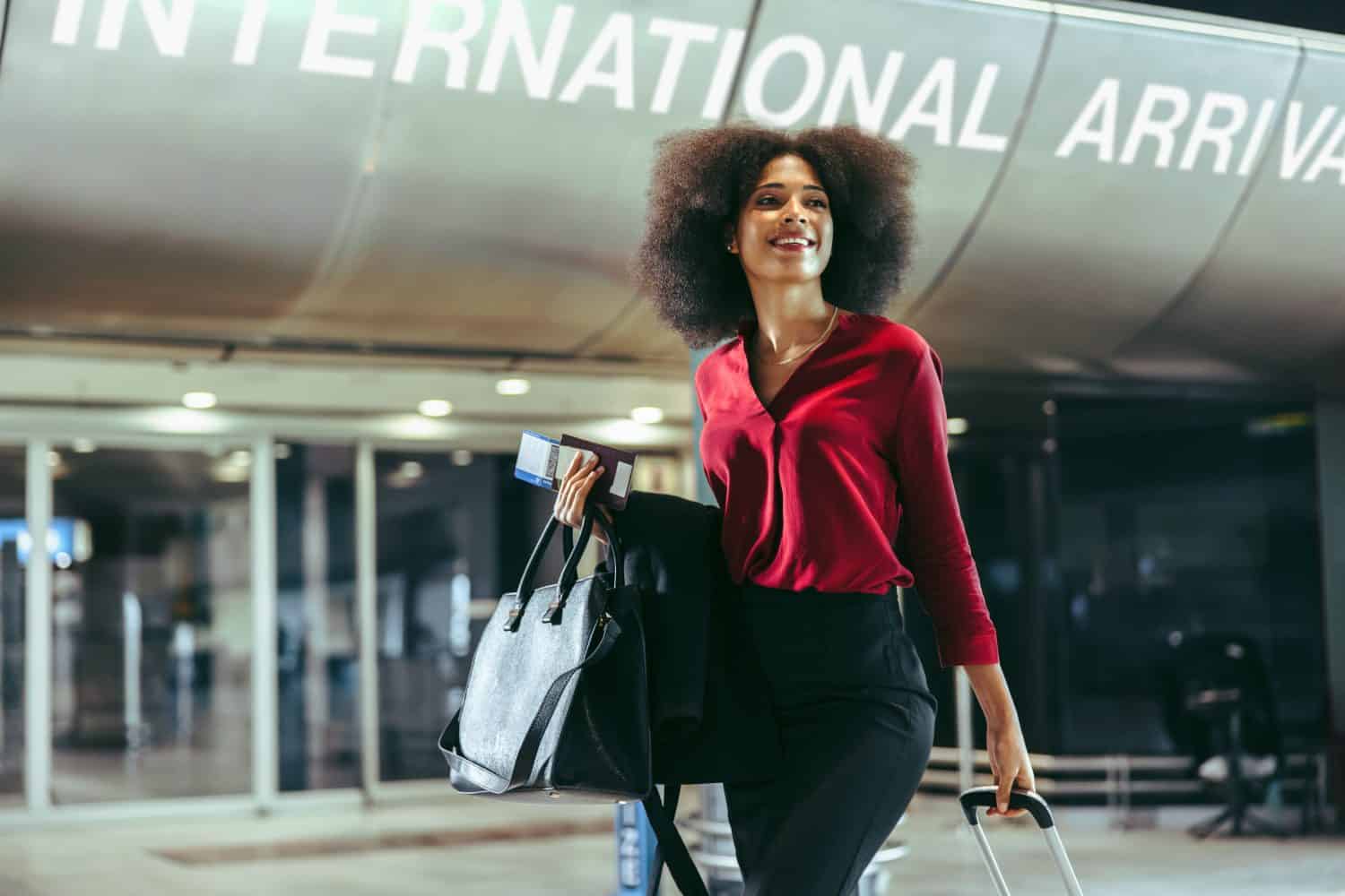 Smiling African woman with luggage walking at international airport. Happy female on international business