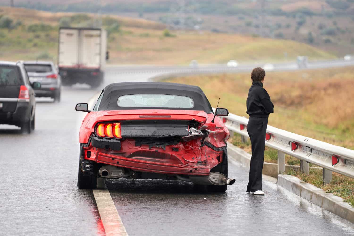 Accident on the road. A broken-down Ford Mustang convertible with a female car driver standing next to it.