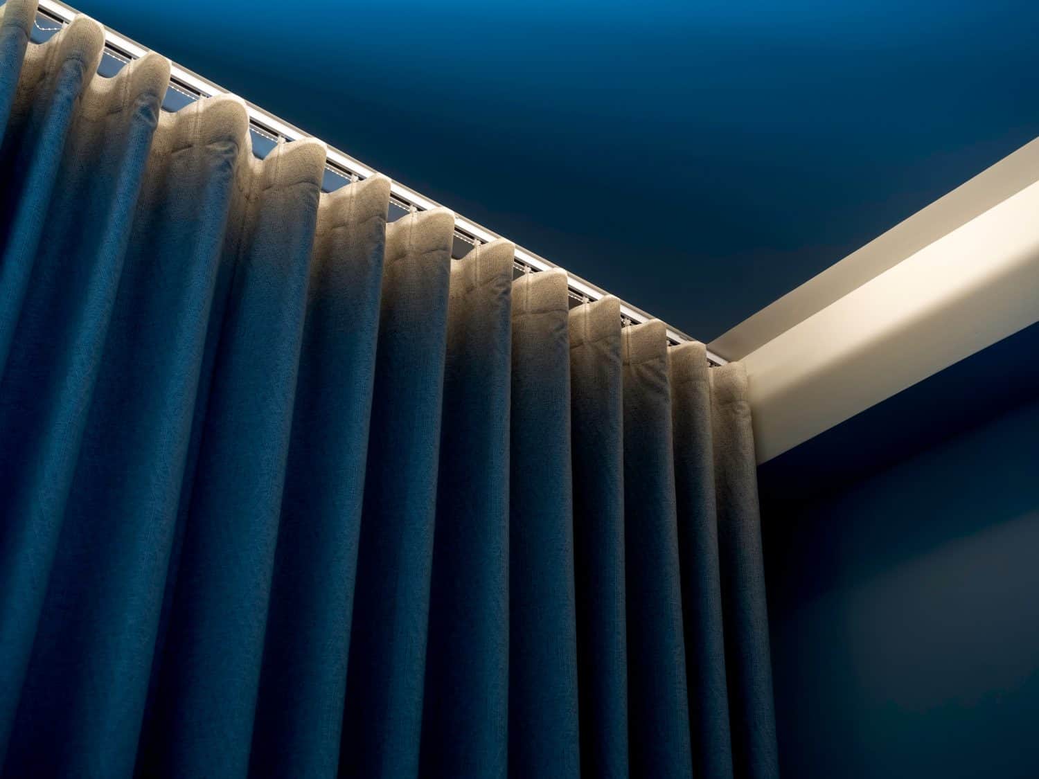 Close-up of blue wall curtain on curtain rail decorated with hidden light under the ceiling near the wall in the blue room corner.