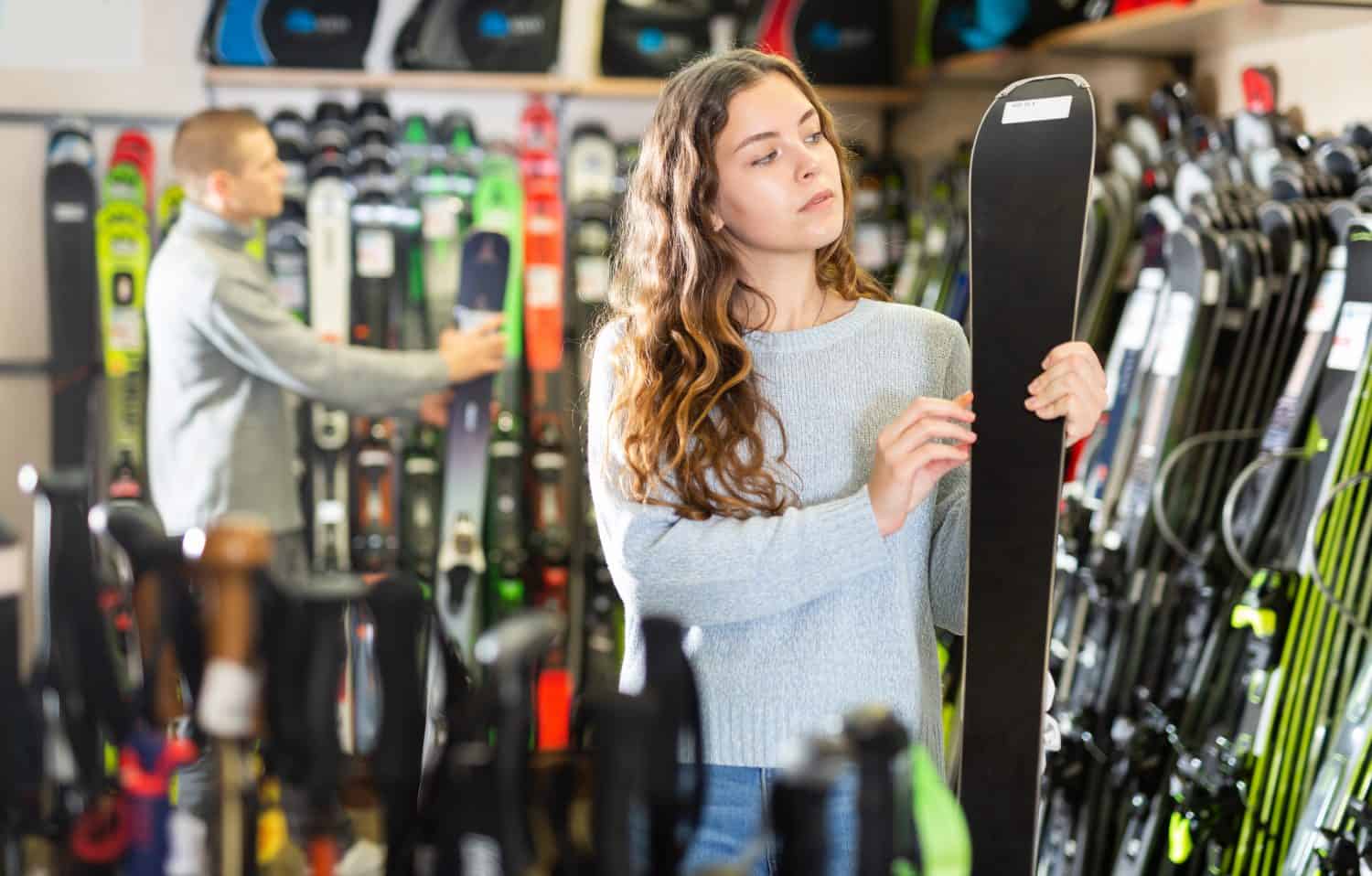 Young couple man and woman make purchase together, choosing new skis in a sport goods store