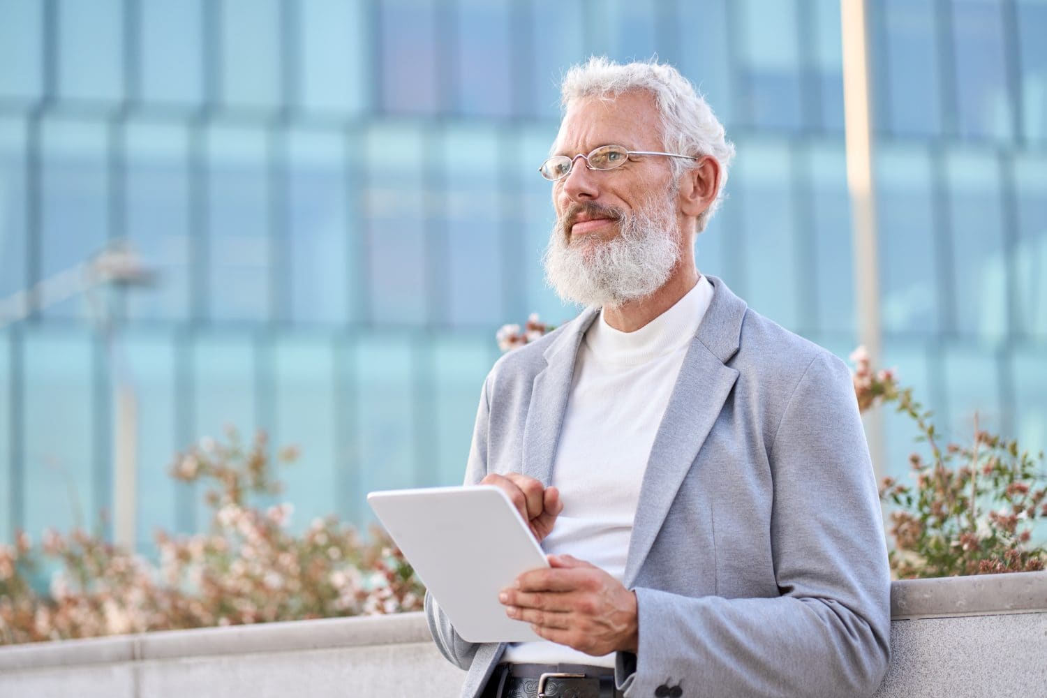 Thoughtful old bearded stylish old mature adult professional business man, senior older businessman ceo wearing suit glasses holding using digital tablet thinking of business ideas standing outdoor.