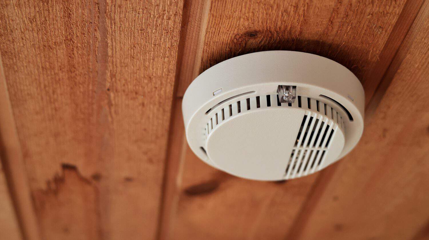 White fire alarm and smoke detector on ceiling in home brown wooden background. Electronic alarms equipment fire protection in building