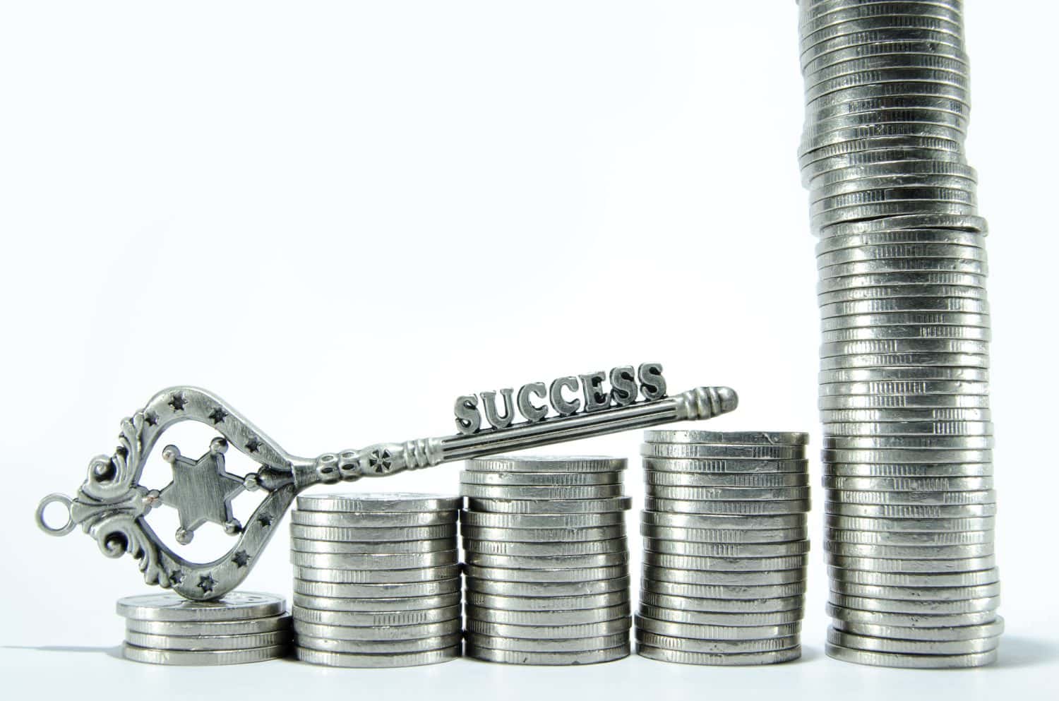 Silver success key on stacked ascending coins on white background, concepts make money grow, success, investing, progress, unlimited growth