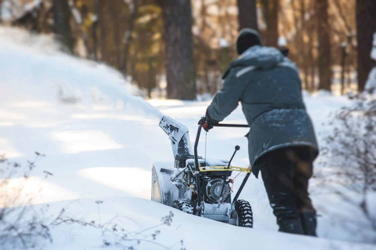 Process of removing snow with portable blower machine, worker dressed in overall workwear with gas snow blower removal in the streets during winter