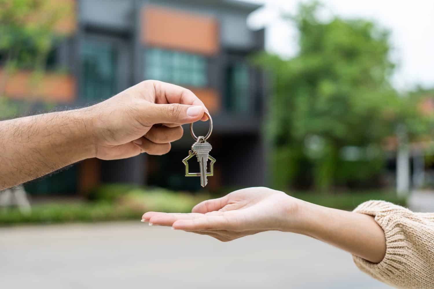 Woman buying or rent new home she holding key front of new house. Surprise happy young asian woman giving house key and smile to rent or purchase apartment home. Moving relocation concept.