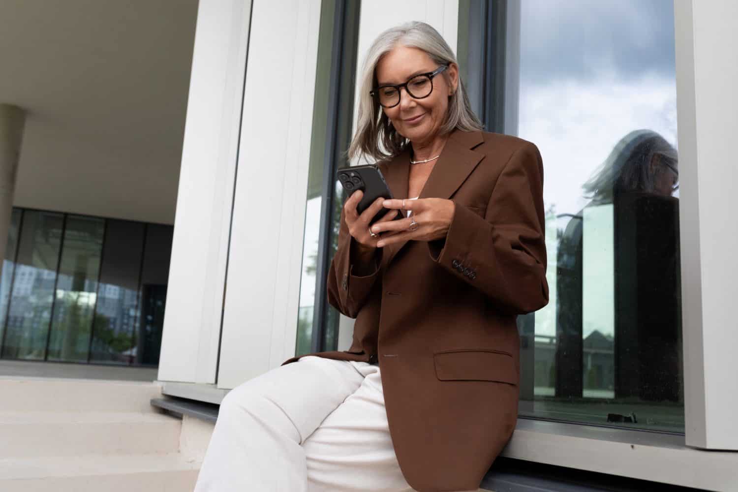 60 year old successful slender gray-haired business woman dressed stylishly checks messages on the mail on the phone