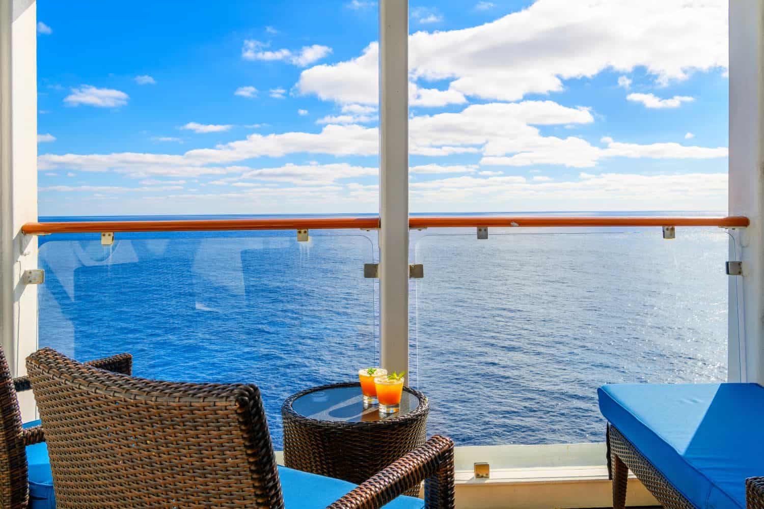 Two tropical mixed alcohol drinks sit on a small end table on the balcony veranda of a cruise ship stateroom on a sunny day on the Mediterranean Sea.