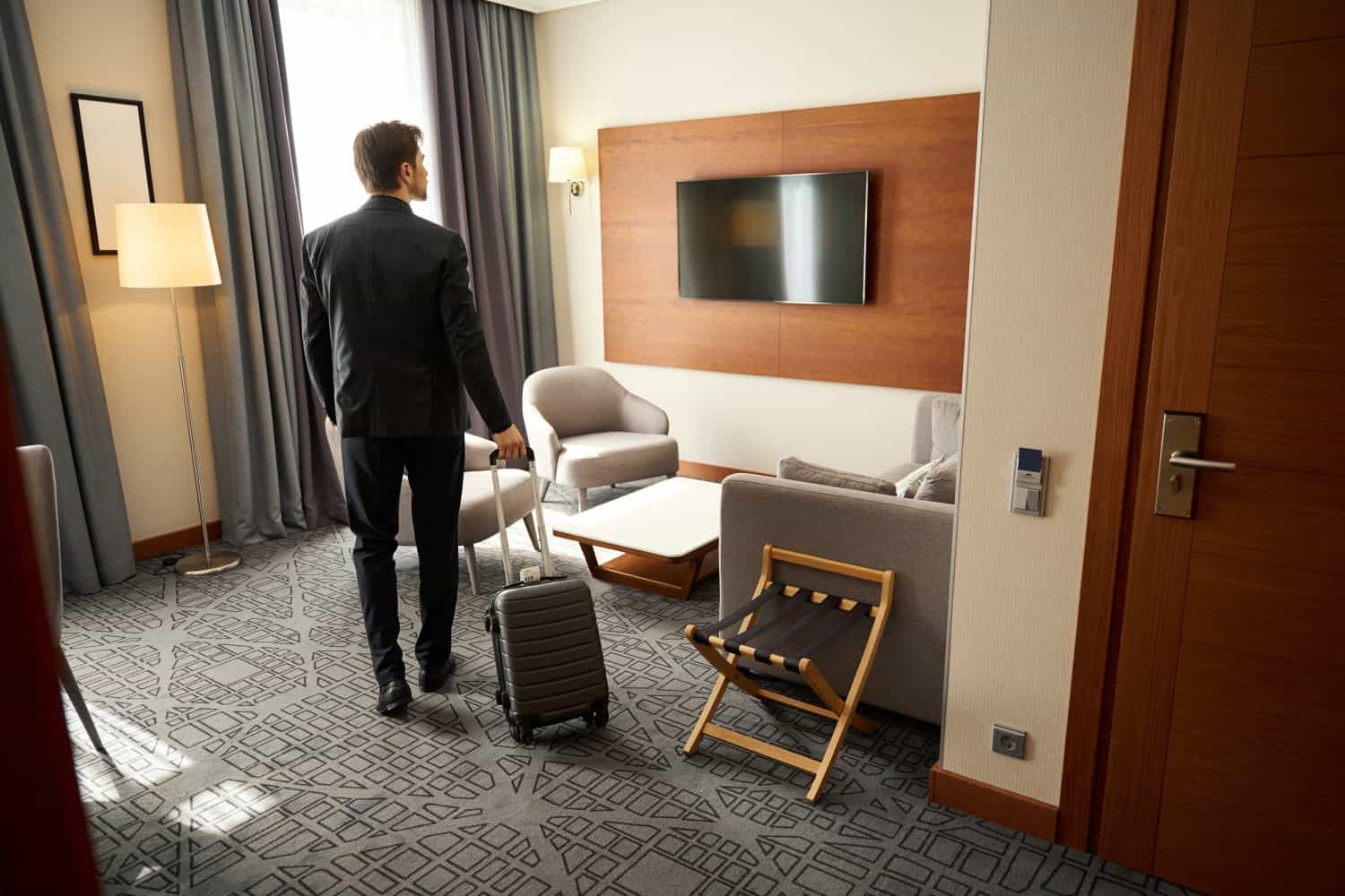 Guy with a travel suitcase stands in a hotel room