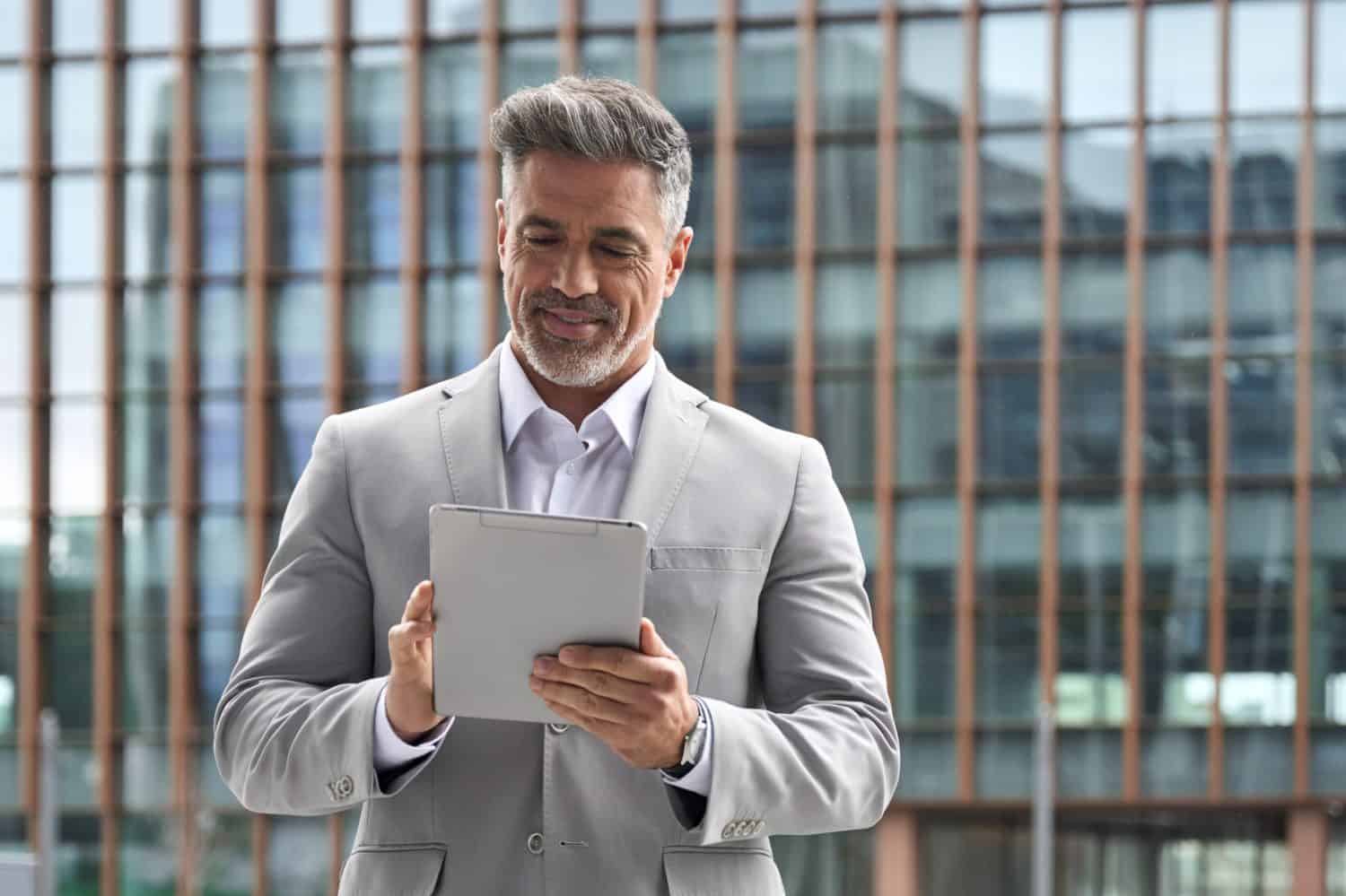 Happy busy middle aged male entrepreneur, rich older investor, confident business man ceo executive leader, mature businessman manager wearing suit using digital tablet investing in banking.