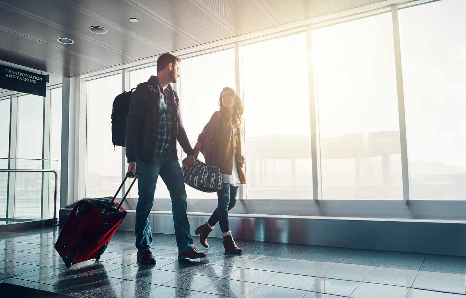 Luggage, travel and walking with couple in airport together for overseas journey, trip or vacation. Holding hands, love or smile with man and woman tourist in lobby, pulling suitcase for boarding