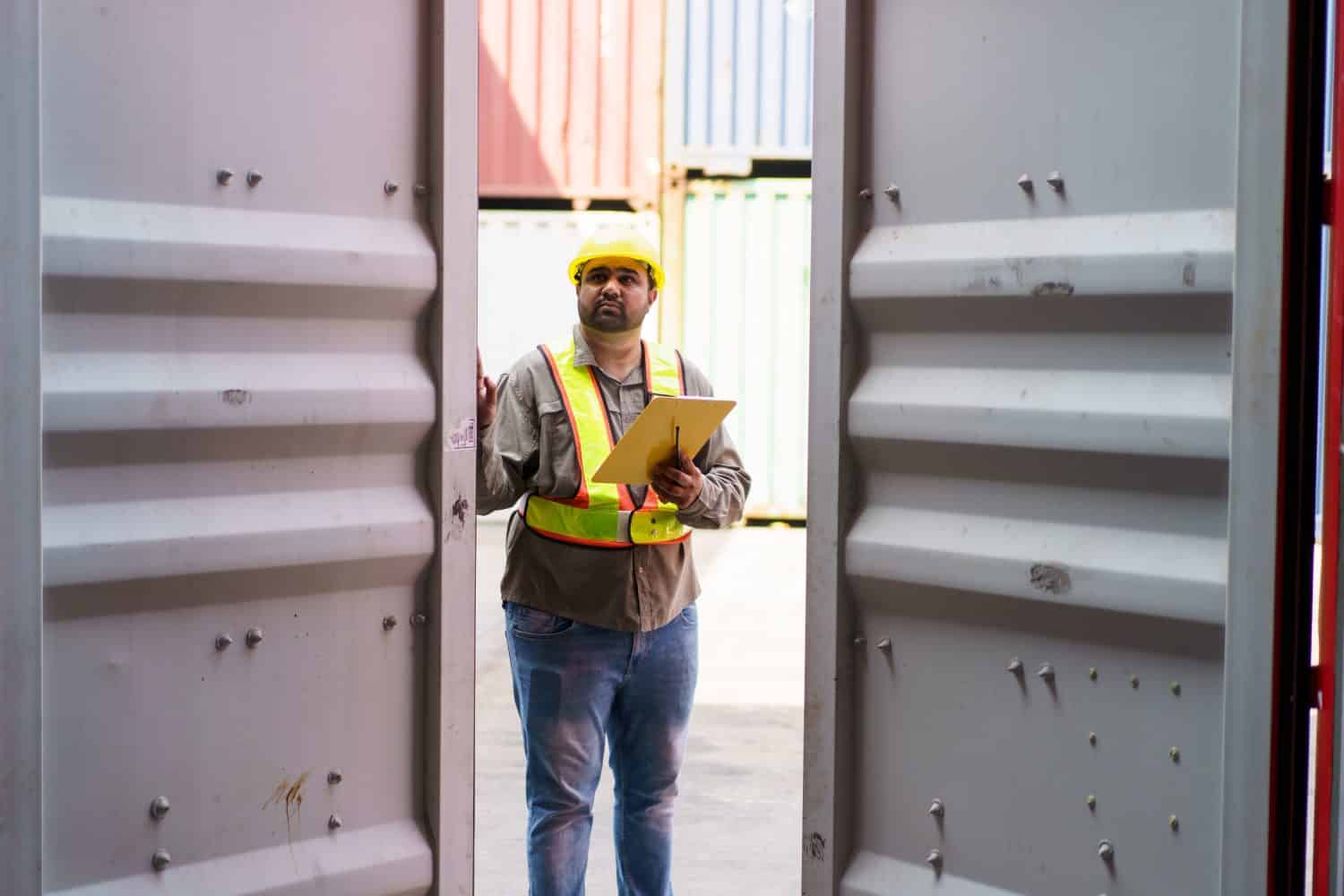 Asian male logistic worker in safety workwear portrait at the container yard. Logistic foreman portrait. Male logistic supervisor is inspecting the incoming cargo container at container yard.