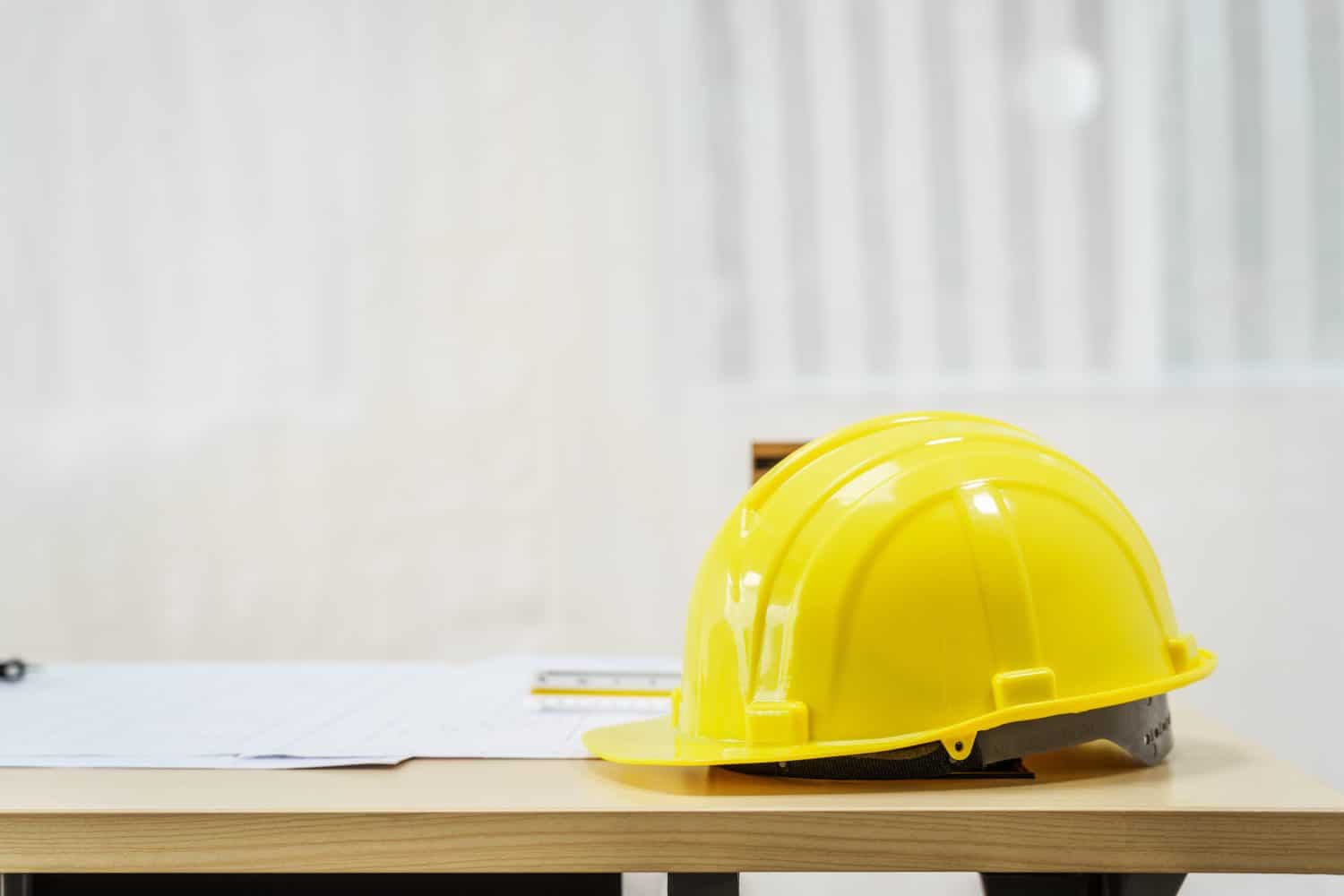 An architect&#039;s desk with blueprints and a white hardhat sits empty, ready for the next project. No people are present, highlighting the tools of the trade.