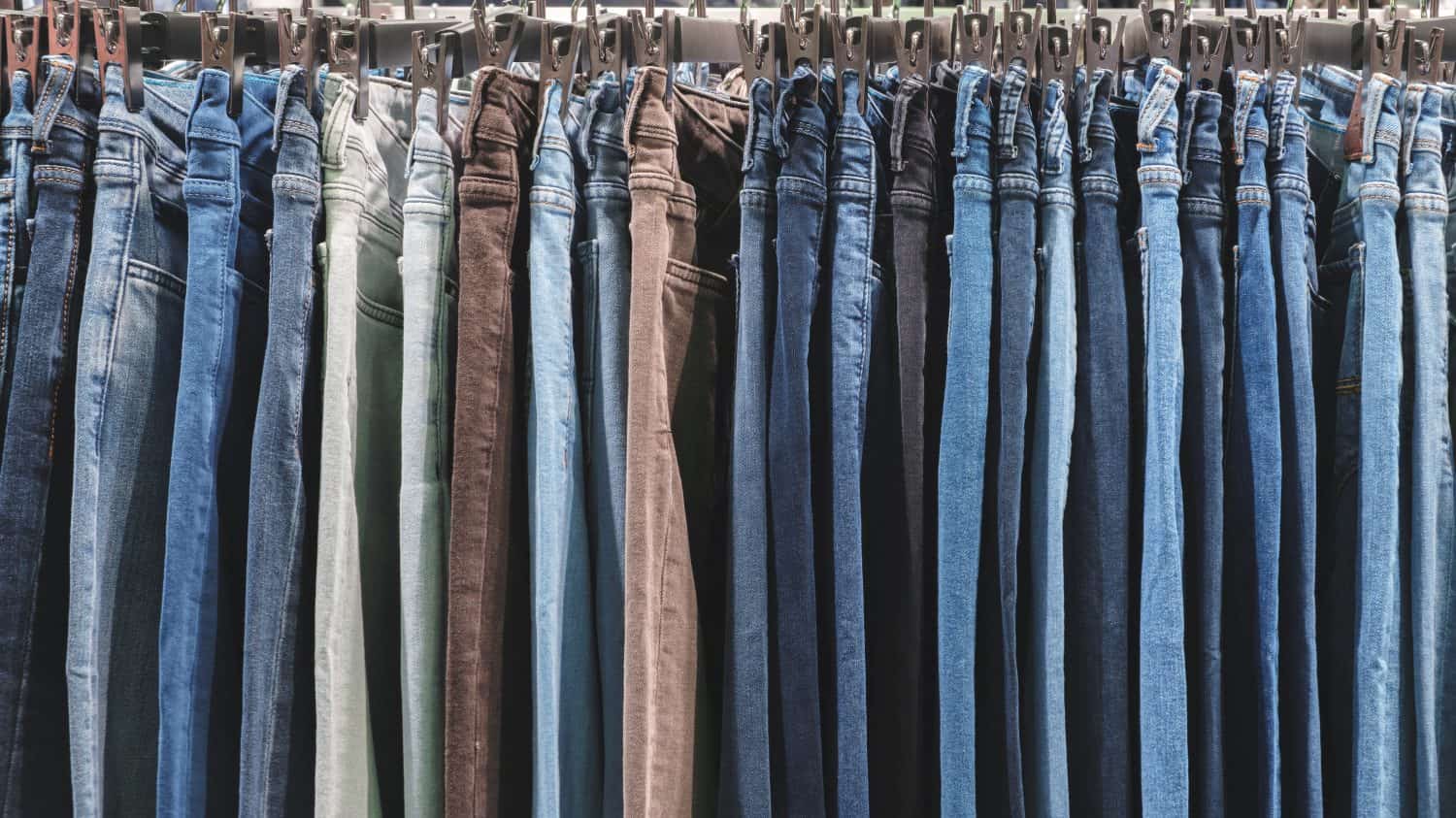 A row of jeans hanging on a rack. The jeans are of different colors and styles. Concept of variety and choice, as the person hanging the jeans can pick from a wide range of options