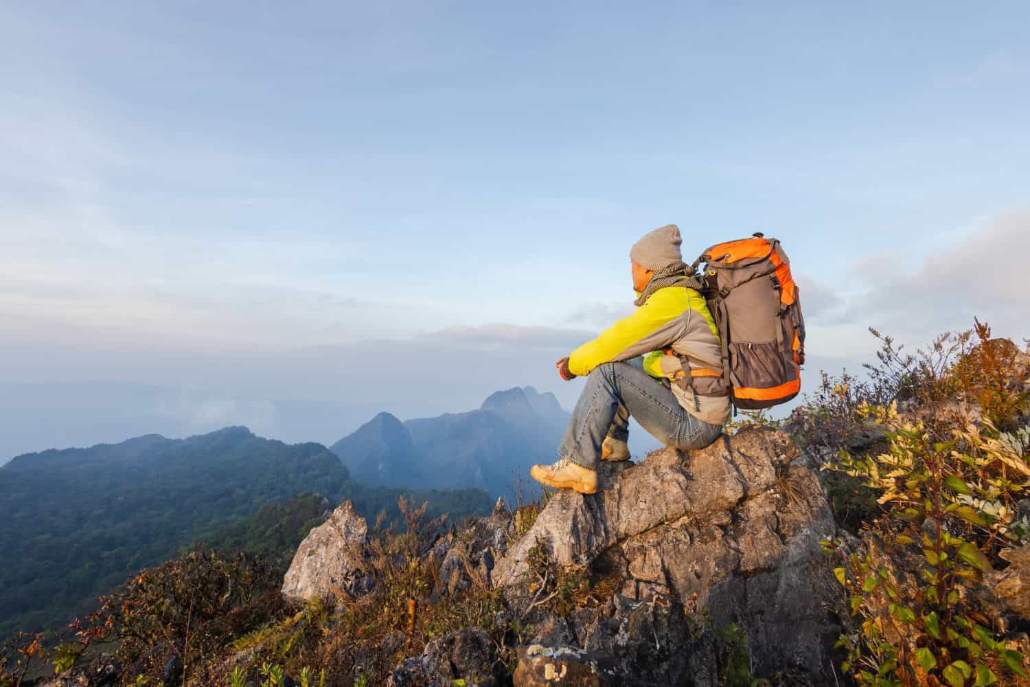 A man is hiking in the mountains with a backpack. He is hiking in the mountains in the morning while the sunlight is soft.