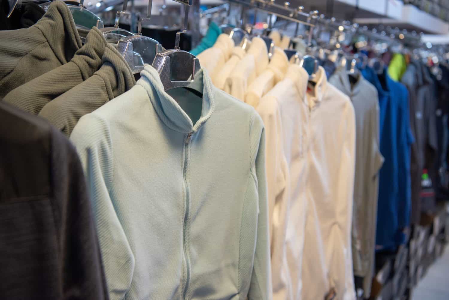 Specialized mountaineering jackets and outdoor apparel in a variety of professional designs and colors displayed neatly on a clothing rack in a dedicated outdoor gear and apparel store.